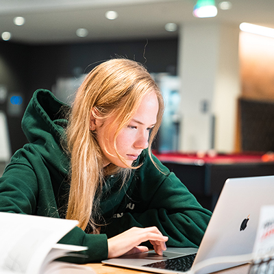 A female student wearing a green hoodie scrolls on the trackpad on a MacBook Air in Lassonde Studios. Image courtesy of the University of Utah.