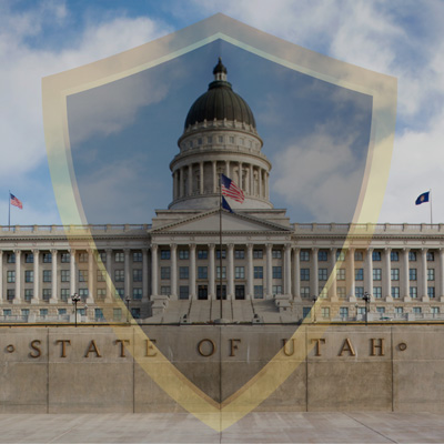 A semi-transparent black shield with a gold outline over the Utah State Capitol.